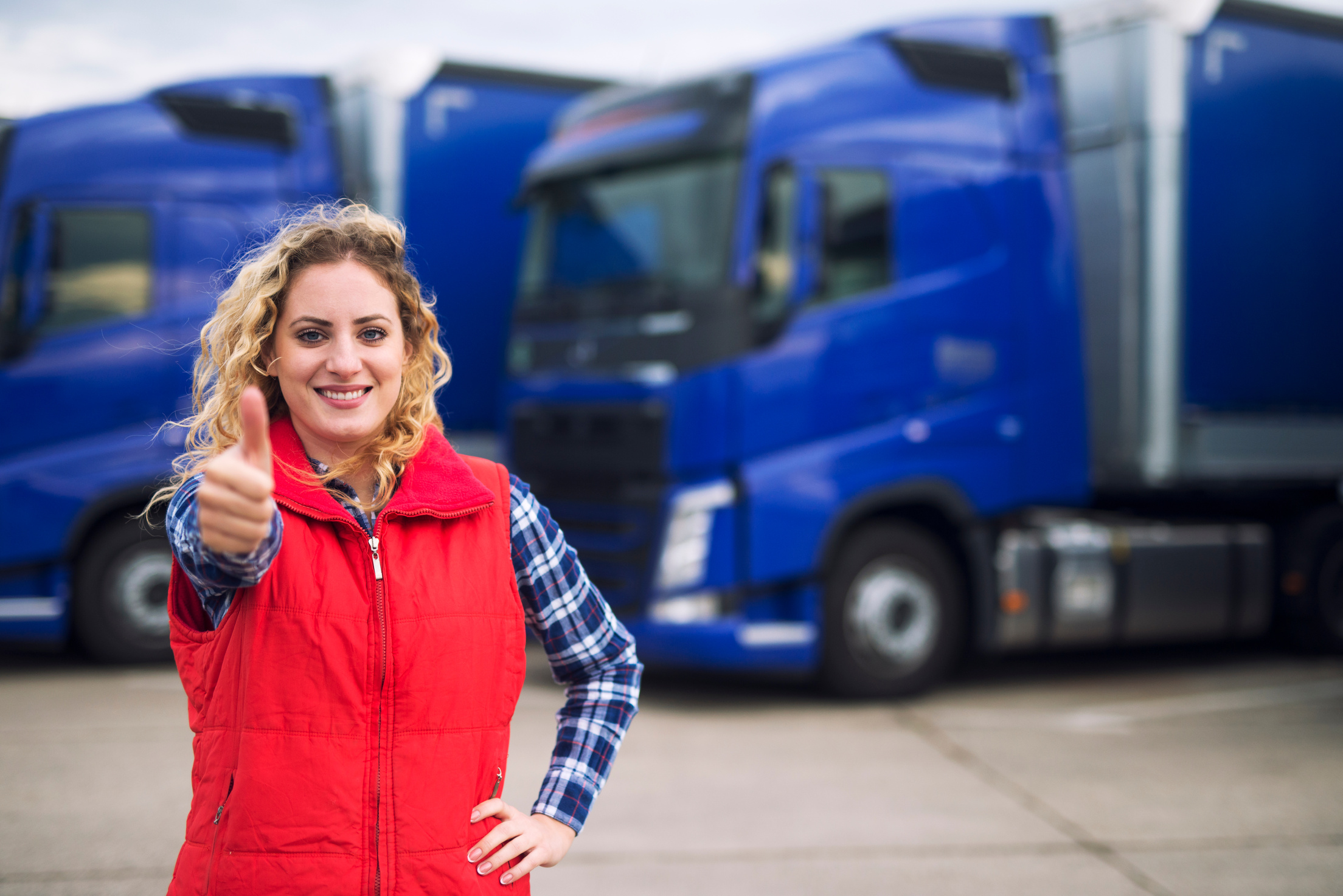 Truck driver occupation. Successful female truck driver in front of transportation vehicles.